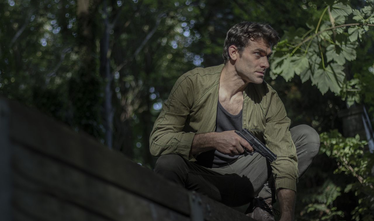 Man crouching with a gun in a forest, displaying alertness and focus.