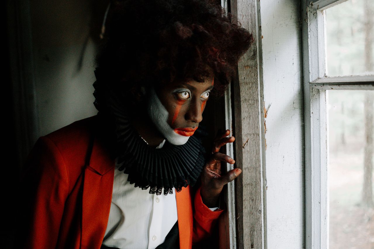 The Art of Drawing Readers In: Your attractive post title goes here A terrifying clown in a dark costume peering out from a dimly lit window, evoking horror and suspense.